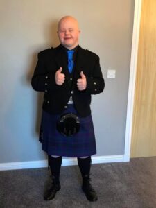 Happy young man wearing traditional Scottish kilt showing thumbs up.